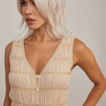 Blonde woman with layered wavy wig in a beige dress, posing indoors.